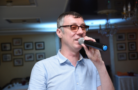 Мужчина в очках и белой рубашке, поёт песню в микрофон